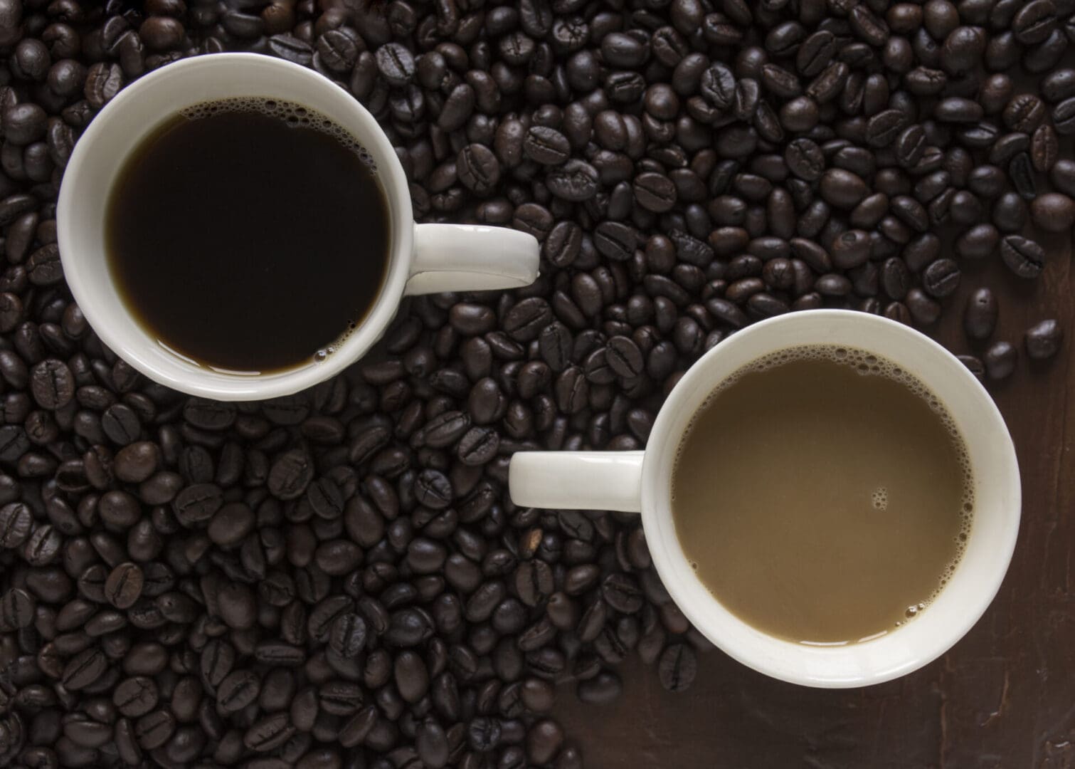 Two cups of coffee versus each other. Dark and milk coffee. On the background coffee beans fade out as they reach to milk coffee. getting less darker.