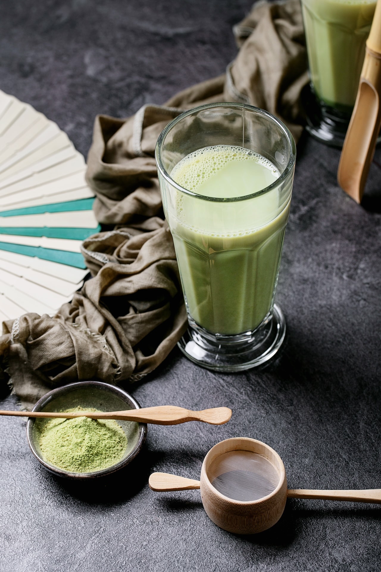 Matcha tea served with matcha powder and bamboo chashaku over dark stone background