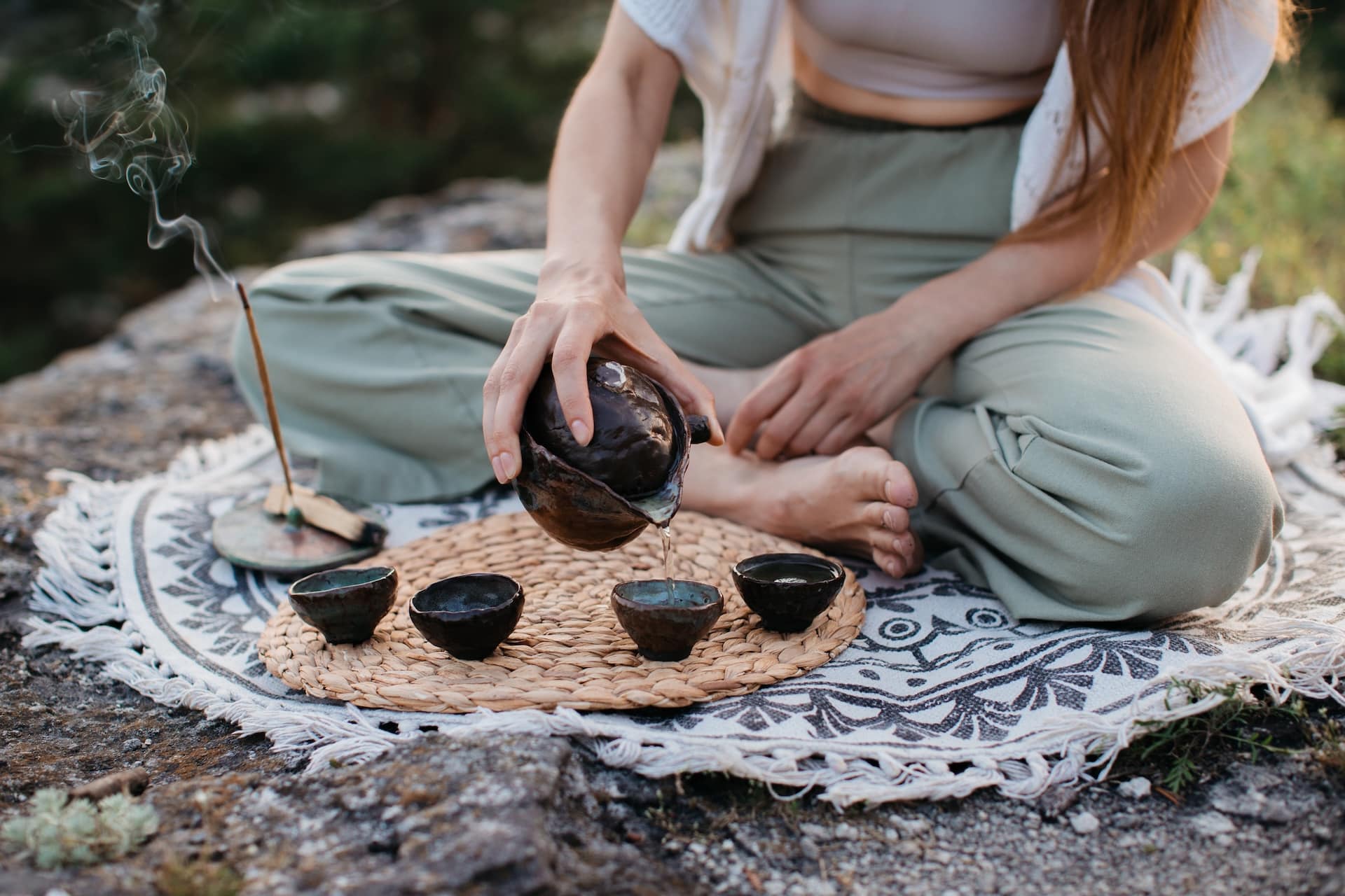 A young beautiful woman performs a Chinese tea ceremony in the mountains at sunset.