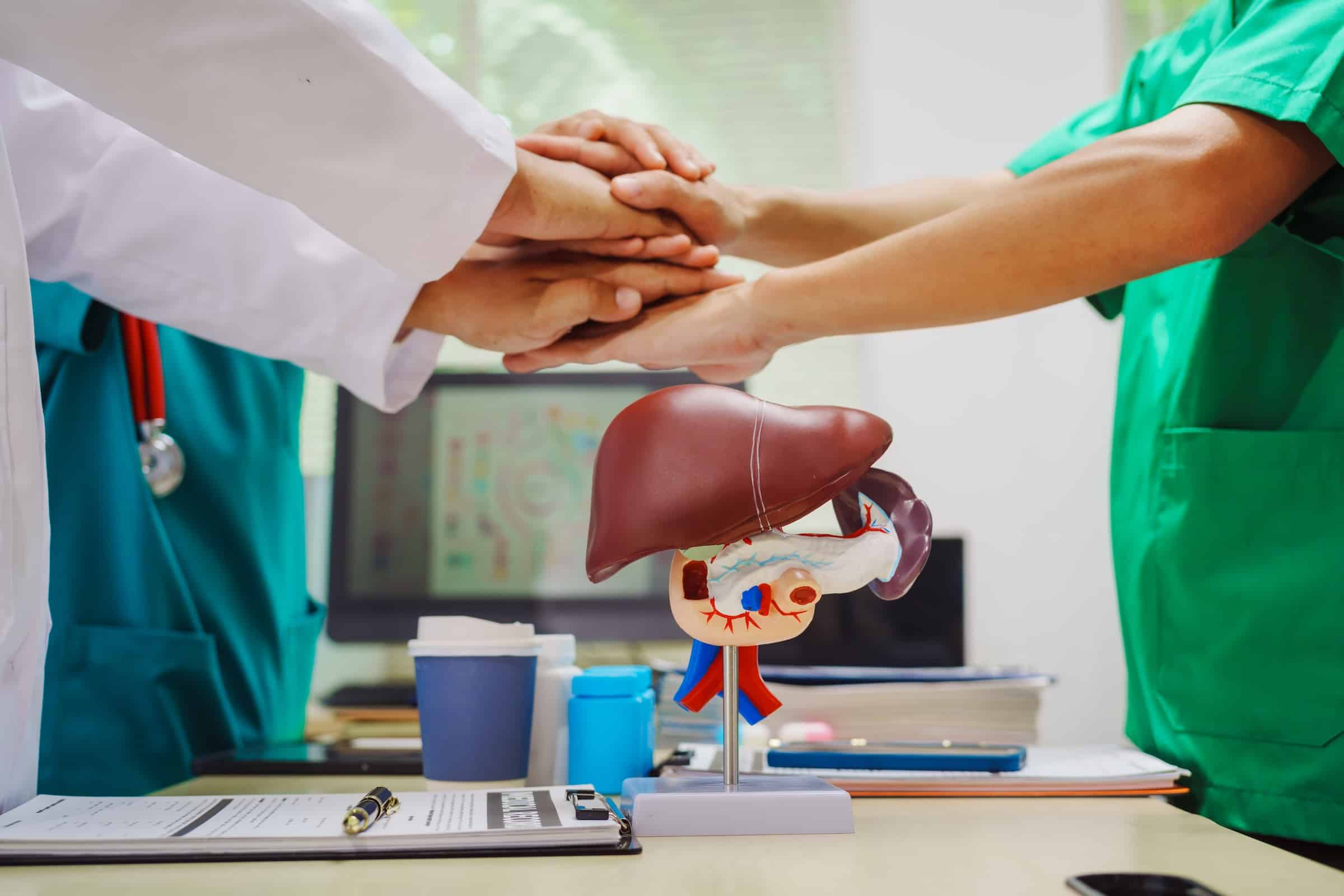 Three doctors join hands at a hospital table after meeting on liver disease,discussing conditions