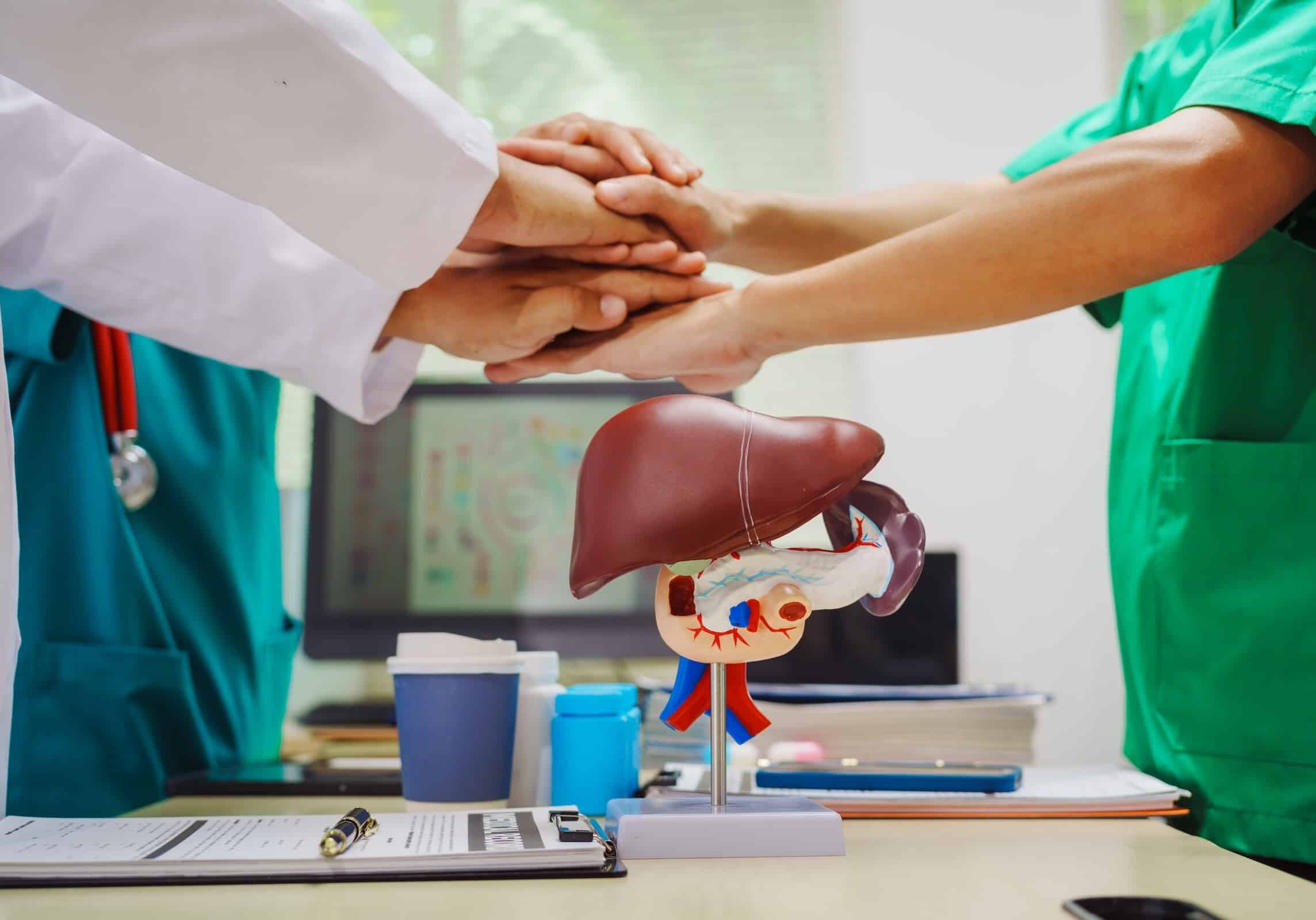 Three doctors join hands at a hospital table after meeting on liver disease,discussing conditions