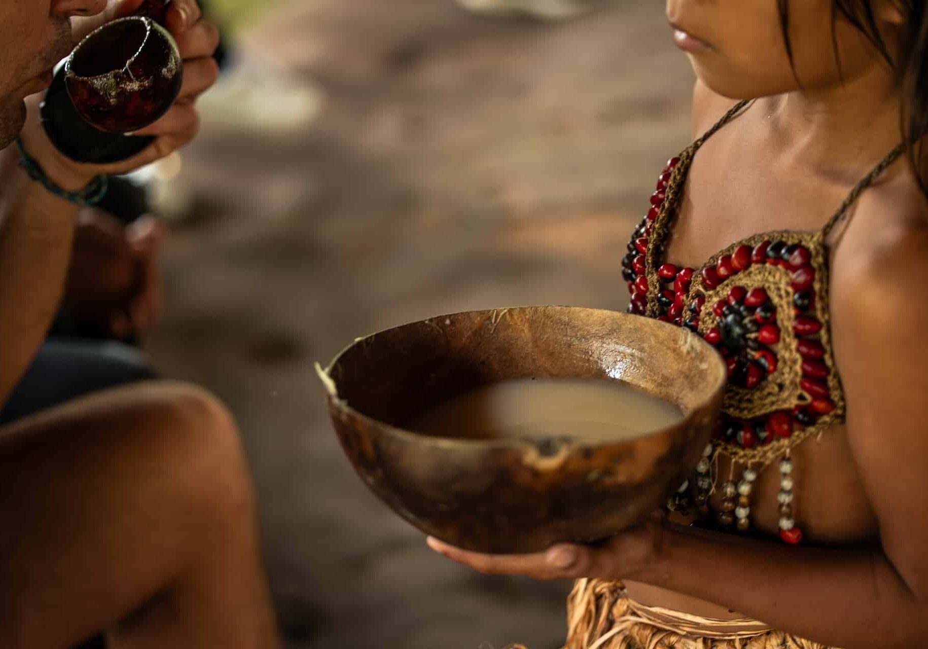 Closeup of a Wayuri indigenous girl presenting a bowl of Chicha drink to a tourist in the Ecuadorian Amazon. This image captures a cultural exchange moment