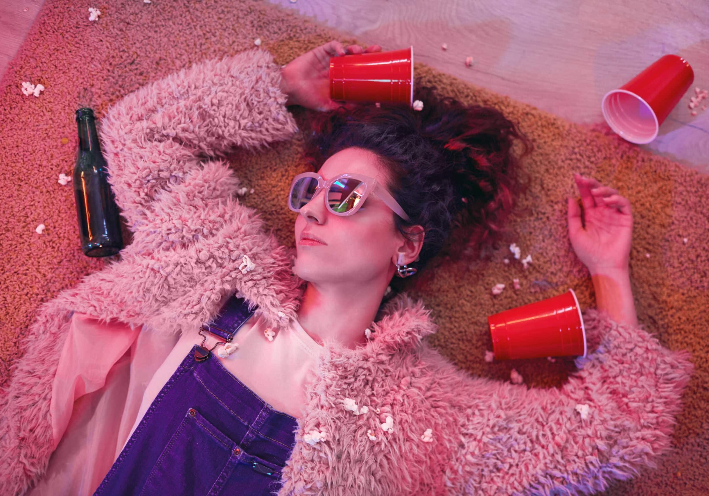 Young woman in sunglasses sleeping on the floor among empty glasses and bottles after party