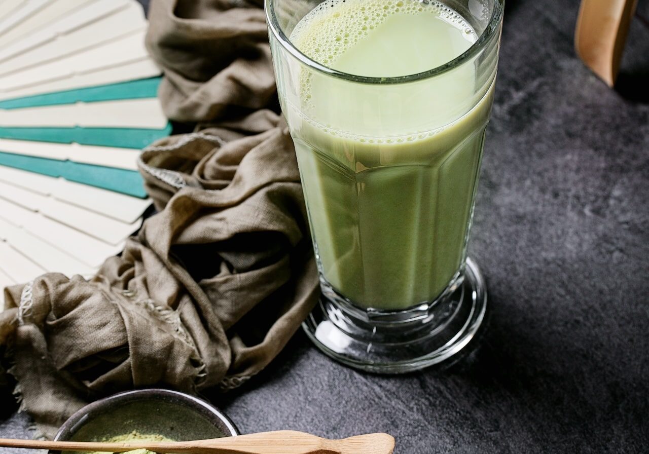 Matcha tea served with matcha powder and bamboo chashaku over dark stone background