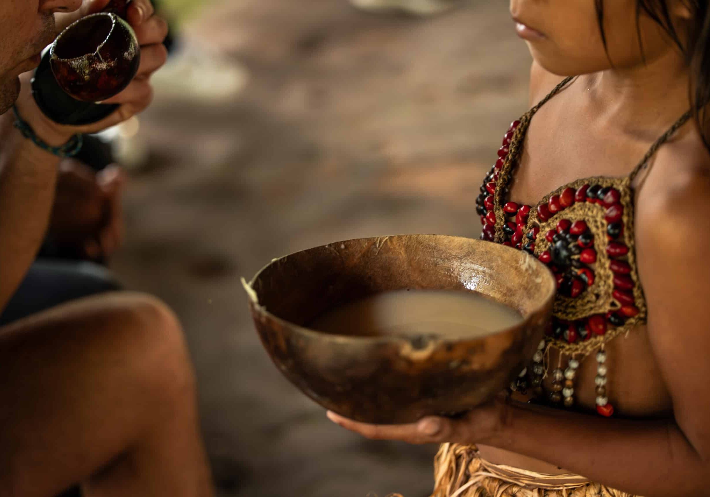 Closeup of a Wayuri indigenous girl presenting a bowl of Chicha drink to a tourist in the Ecuadorian Amazon. This image captures a cultural exchange moment